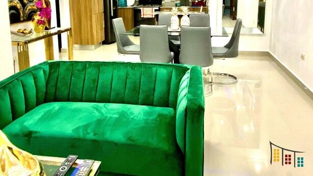 Un salon moderne avec un canapé vert, un coin repas avec une table et des chaises, et une cuisine en arrière-plan.