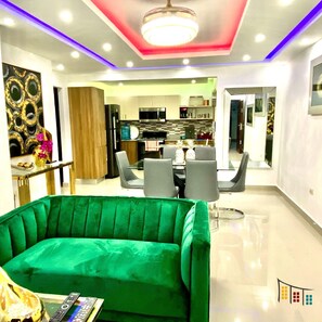 Un salon moderne avec un canapé vert, un coin repas avec une table et des chaises, et une cuisine en arrière-plan.