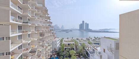 A high-rise hotel with multiple balconies, a rooftop pool, and a view of the sea and city skyline.
