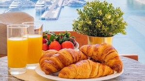 A breakfast setting with croissants, orange juice, and strawberries on a table with a city view. - EDEN'S Homes & Villas - FIVE Residences (Dubai)