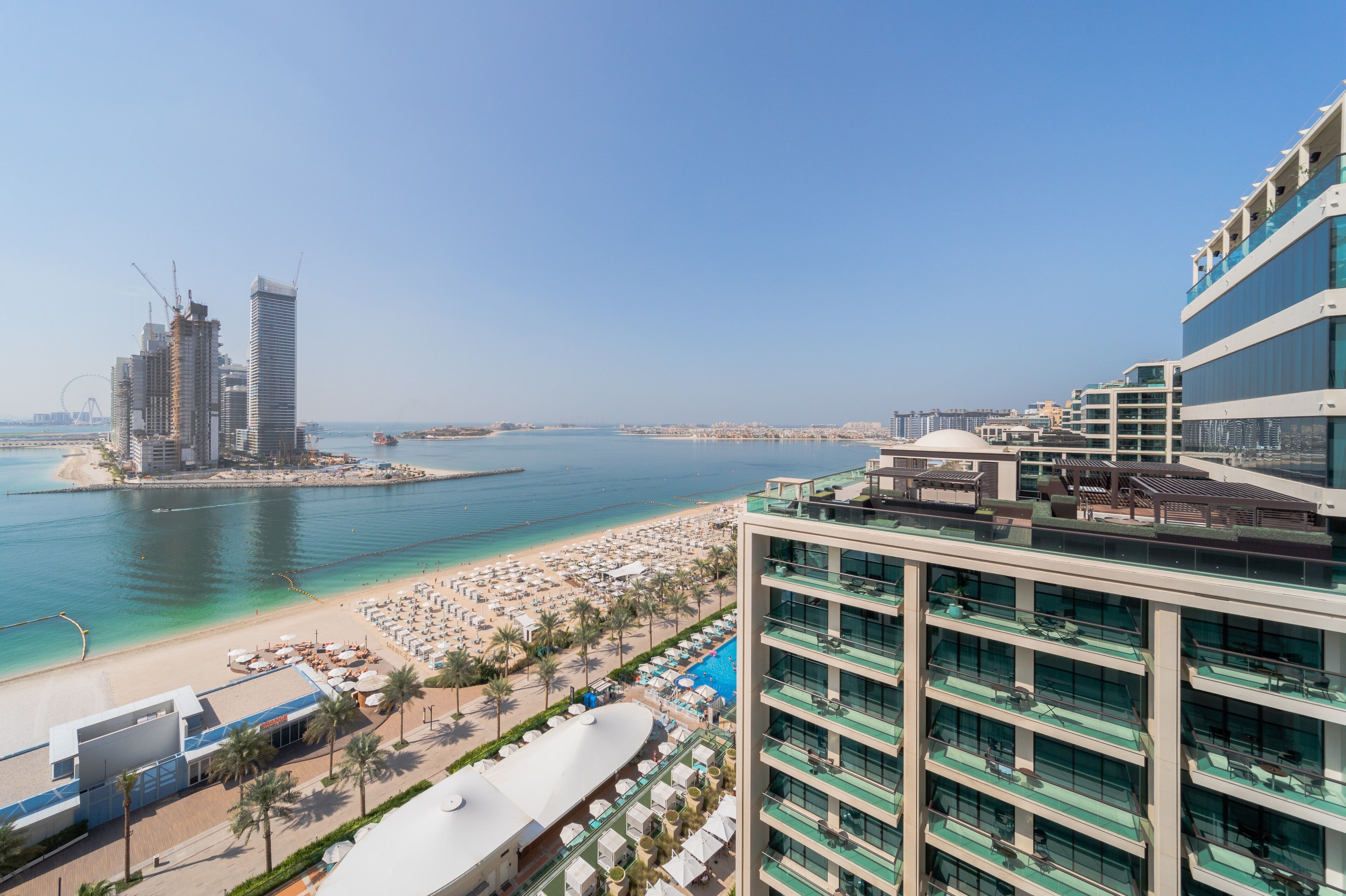 A high-rise hotel with multiple balconies overlooking a beach and marina.