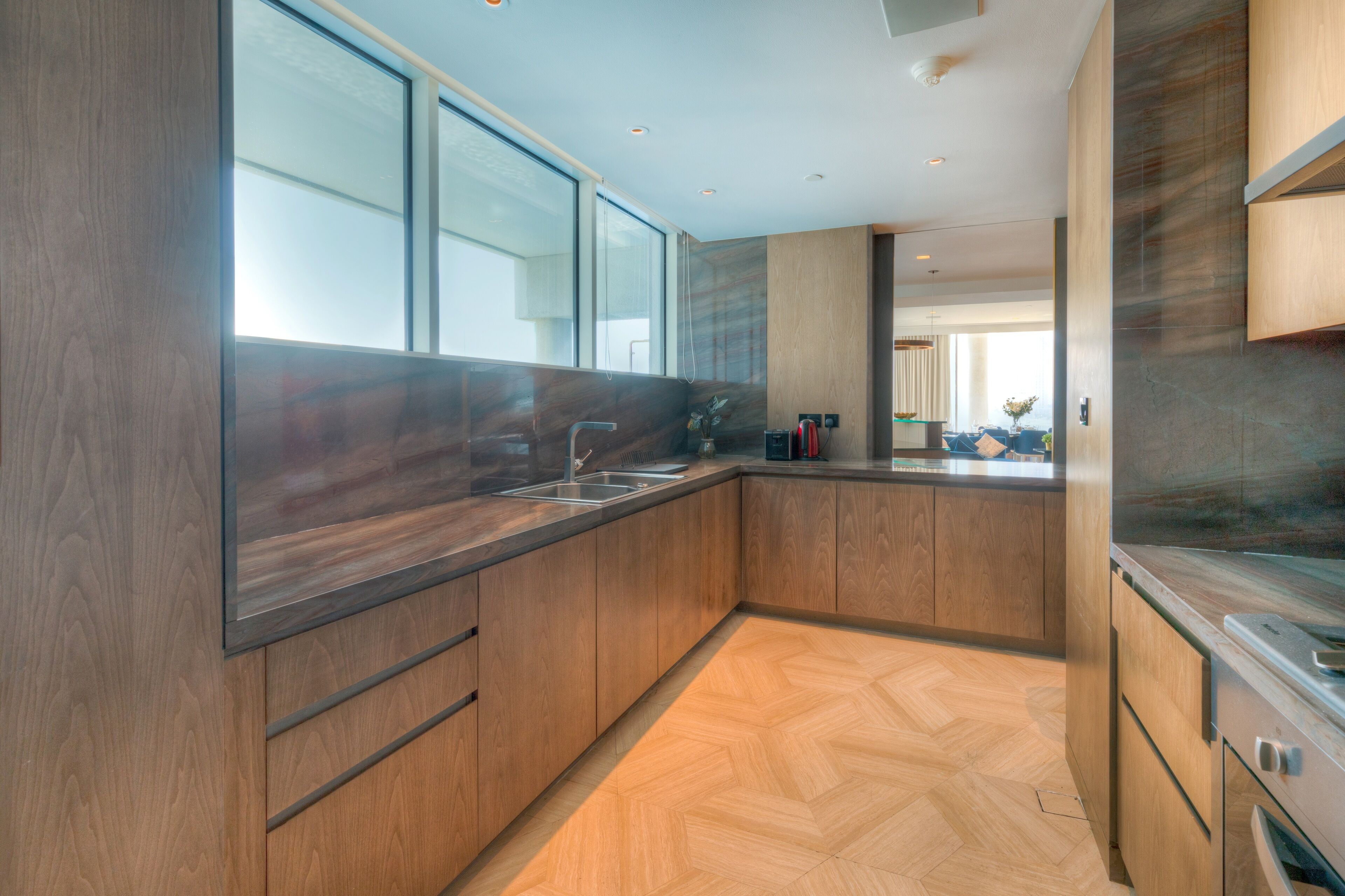Une cuisine moderne avec des meubles en bois, un évier en acier inoxydable et un sol à motifs en chevrons.
