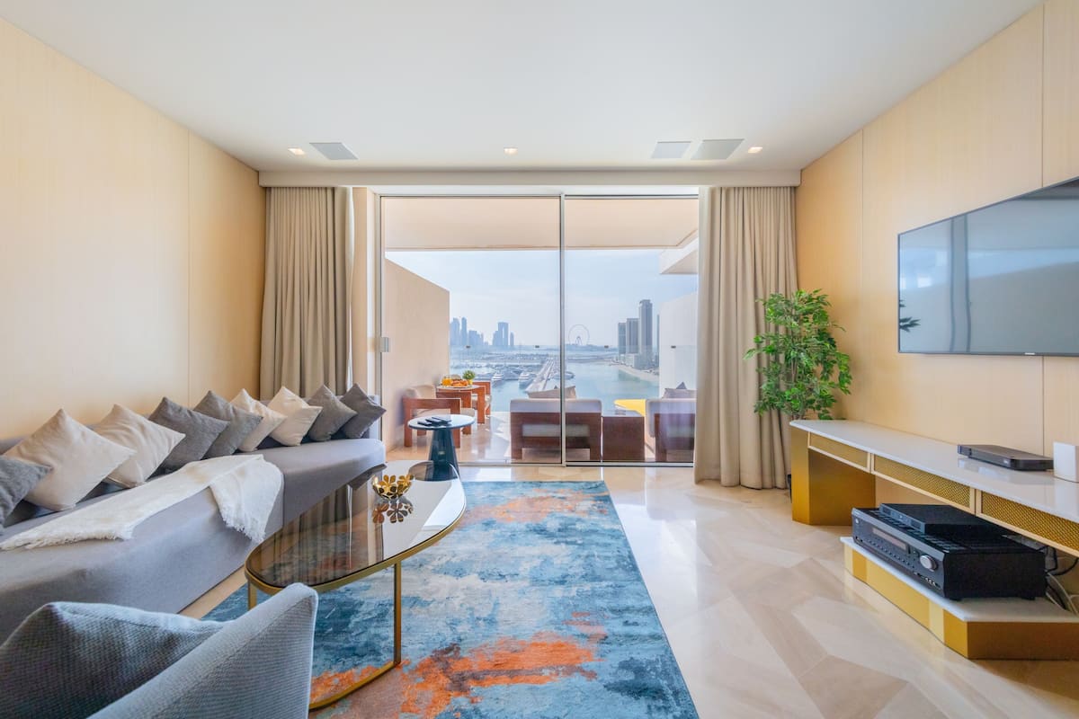 Una sala de estar moderna con sofá, mesa de centro y mueble de entretenimiento. Un amplio ventanal ofrece vistas de la ciudad.