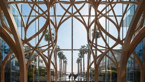 A modern atrium with a geometric wooden framework and glass walls, reflecting the surrounding palm trees and sky. - EDEN'S Homes & Villas - FIVE Residences (Dubai)