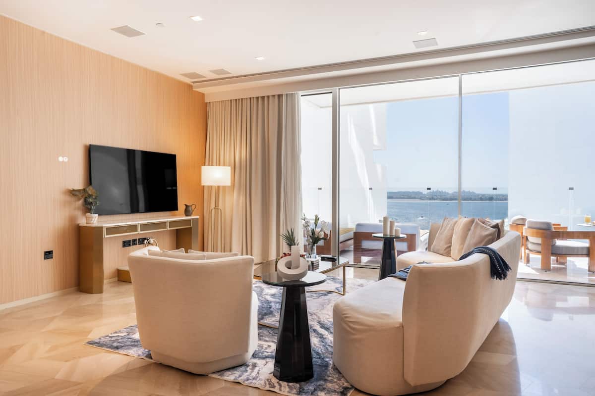 Una sala de estar moderna con televisor de pantalla plana, dos sofás, una mesa de centro y un ventanal con vista al mar.