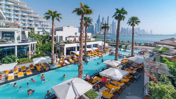 A resort pool area with multiple levels of balconies, palm trees, and a view of the city skyline. - EDEN'S Homes & Villas - FIVE Residences (Dubai)