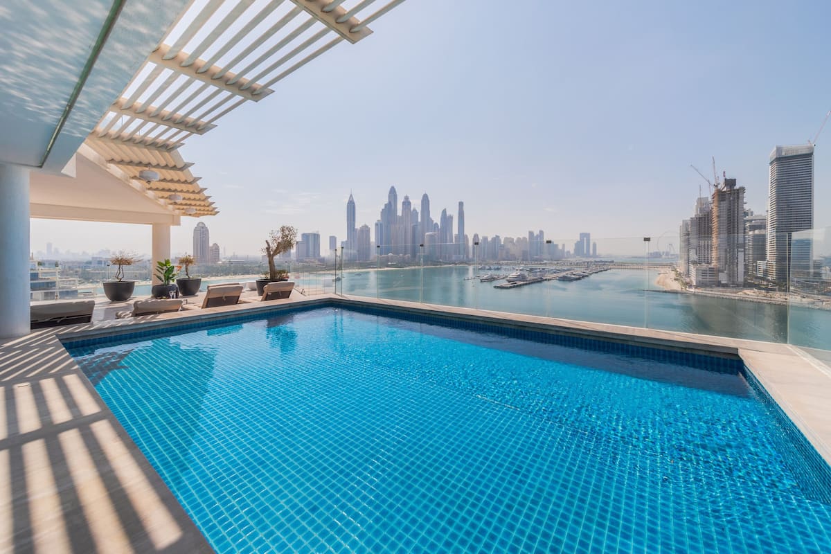 Una piscina en la azotea con vista al horizonte de la ciudad, que incluye edificios altos y un puerto deportivo.
