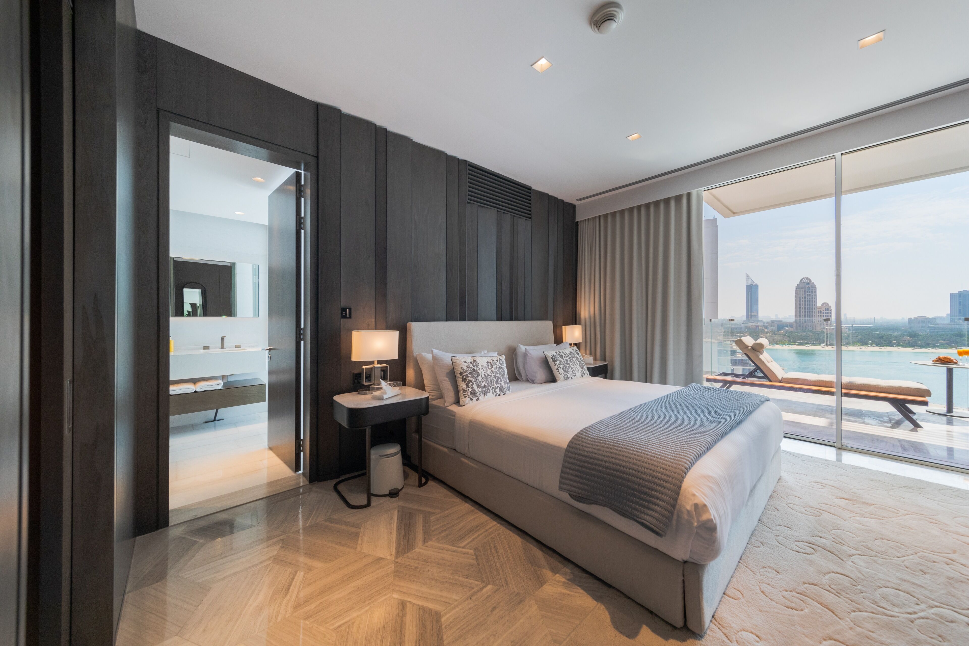 Une chambre d’hôtel moderne dotée d’un grand lit, d’une salle de bain avec miroir et d’un balcon offrant une vue sur la ville.