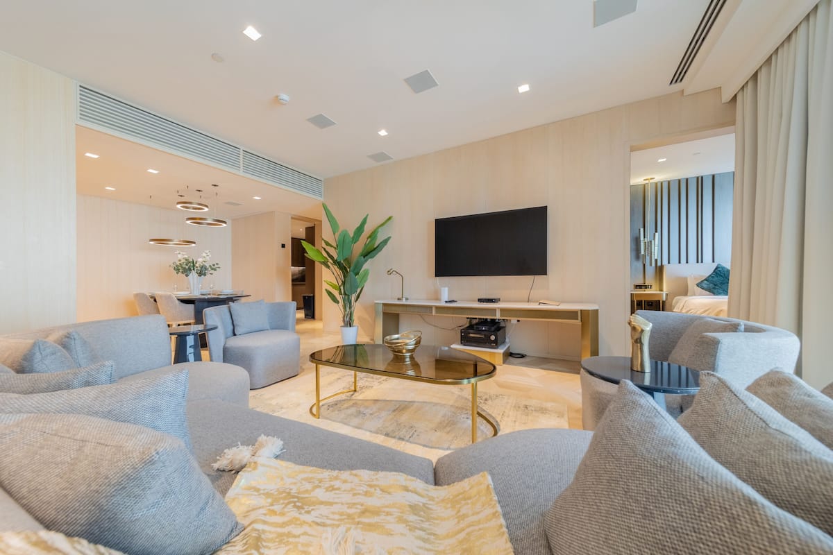 Una sala de estar moderna con sofás grises, una mesa de centro de vidrio, un televisor de pantalla plana y un comedor con una mesa y sillas.
