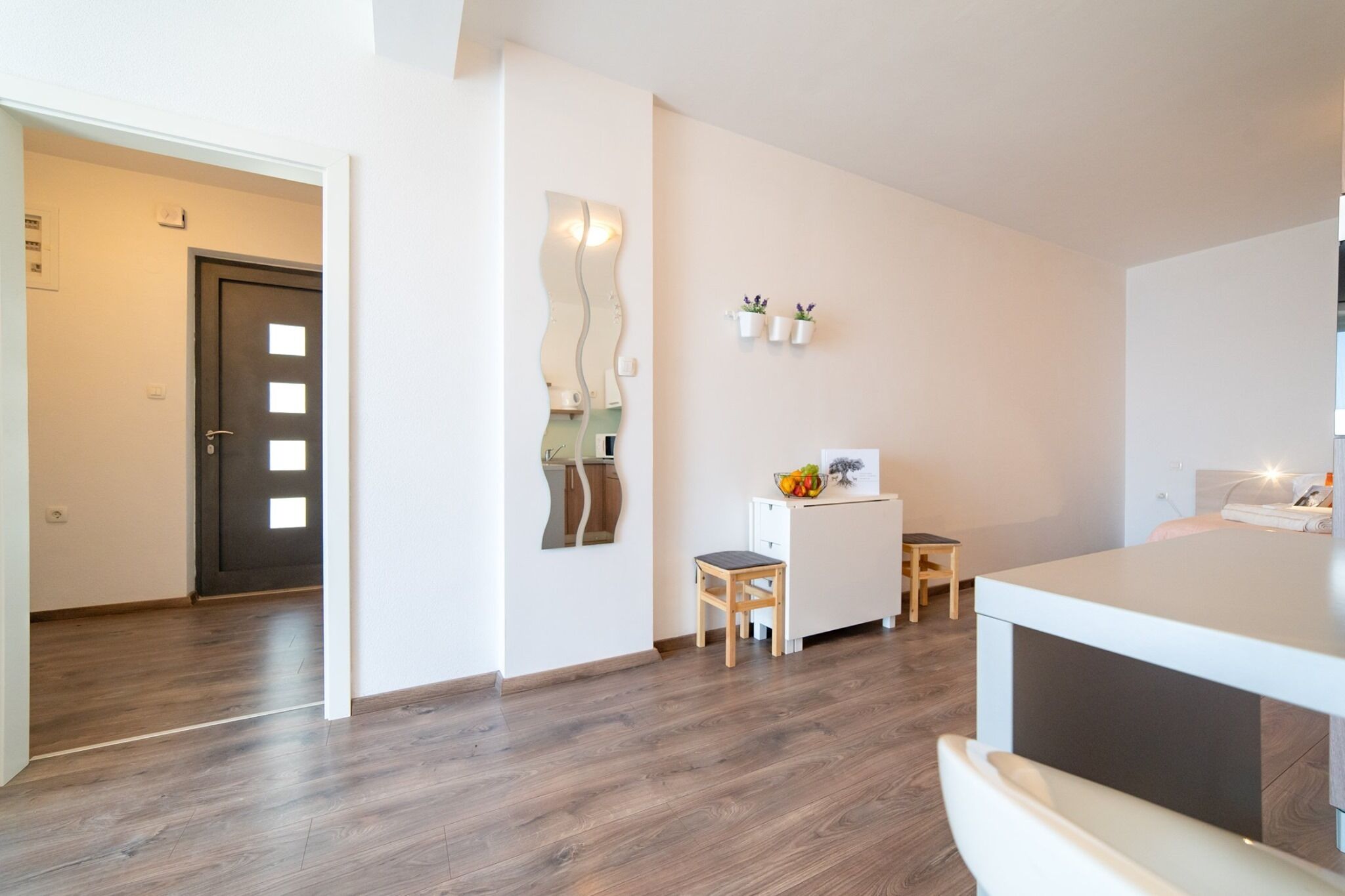 A modern kitchen with a white countertop, wooden stools, and a small table.