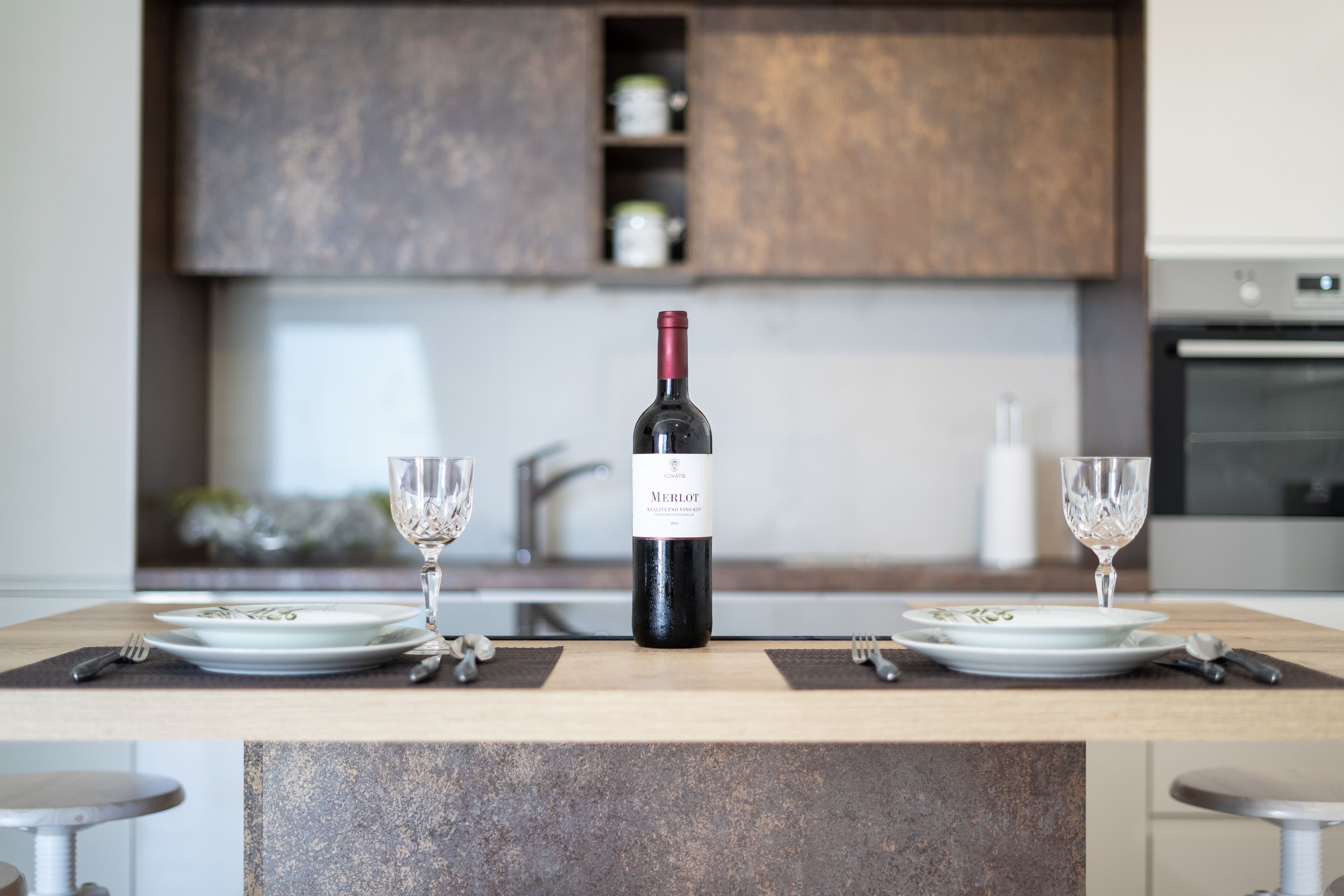 Una cocina moderna con una isla central, dos copas de vino y una botella de vino Merlot.