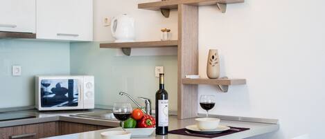 A modern kitchen with white cabinets, a built-in microwave, a wine bottle, and a fruit bowl.