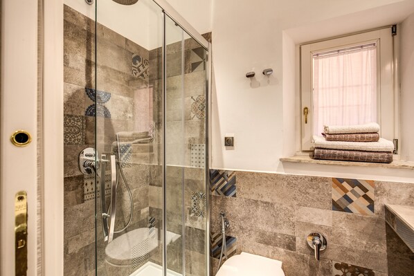 Un baño moderno con ducha de vidrio, un lavamanos y una ventana con perchero para toallas.