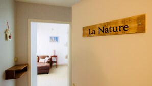 A wooden sign with "La Nature" on a beige wall, a brown sofa, a small table, and a picture frame in a room. - VéloGîtes, Le Gîte de la Nature, the perfect place for a family vacation? (Availles-Limouzine)