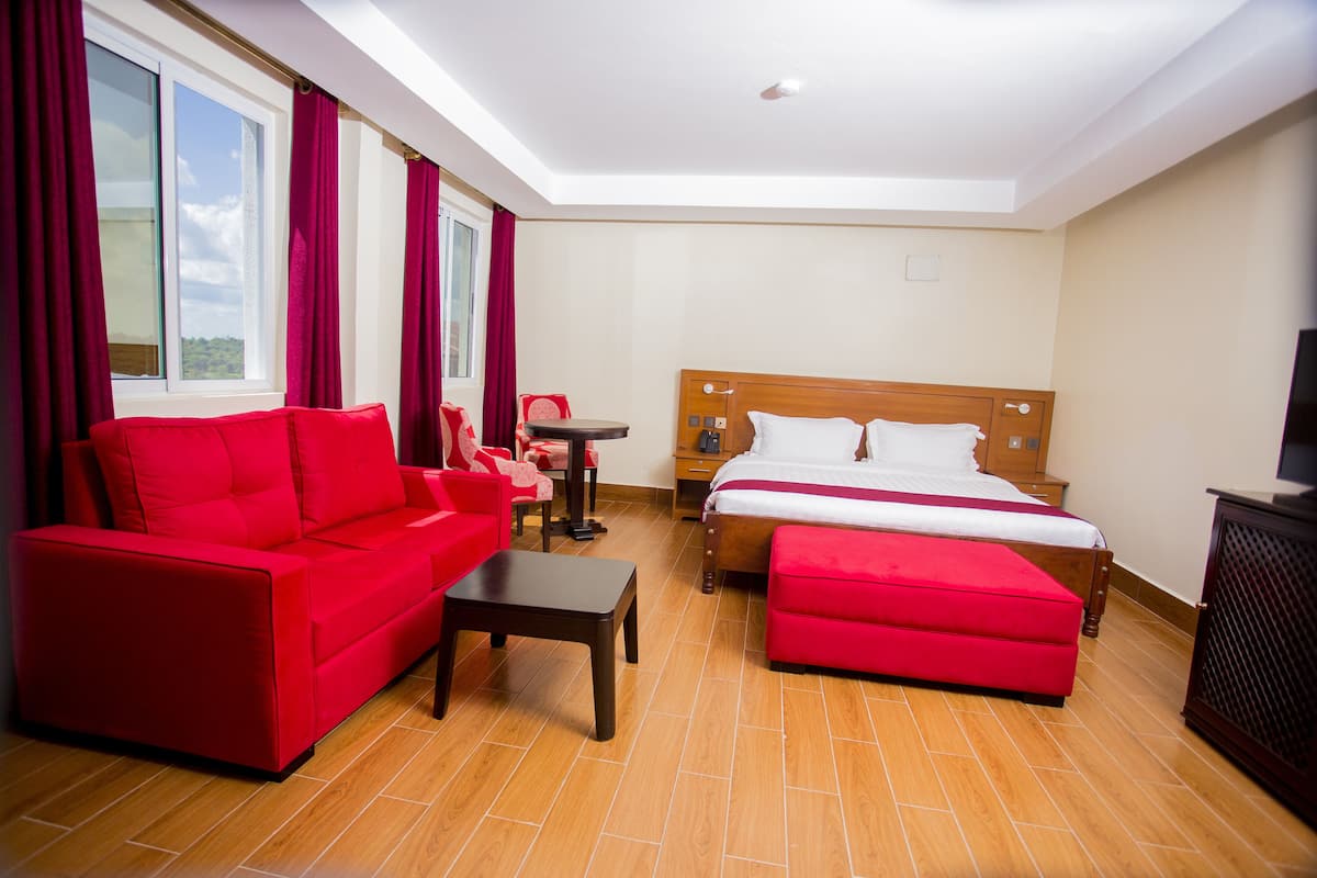 A hotel room with a red sofa, a wooden bed, a small table, and a TV.