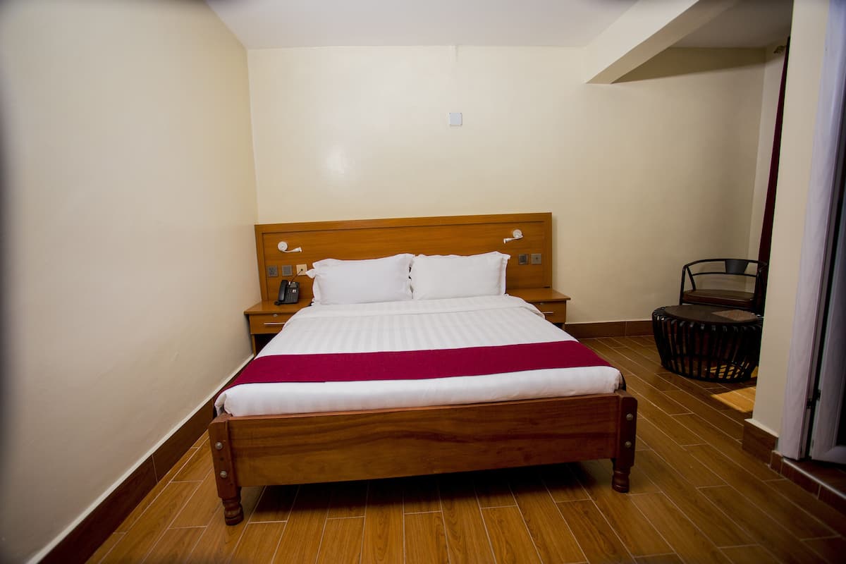 A neatly made bed with a wooden headboard, a bedside table with a lamp, and a small round table with a chair.