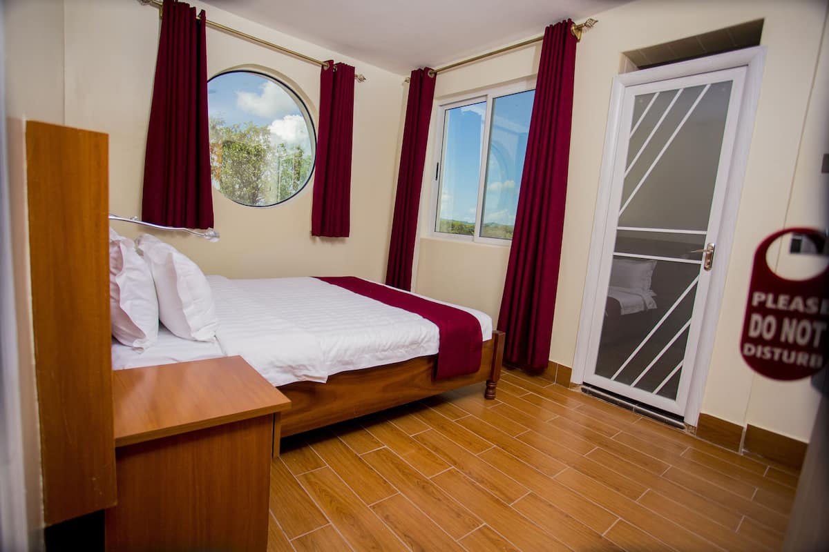 A bedroom with a wooden bed, a window with curtains, a door with a sign, and a tiled floor.