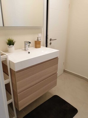 A bathroom with a white sink, wooden cabinet, and a small potted plant.