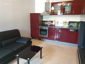 A compact kitchen with red cabinets, a stainless steel stove, and a black countertop.