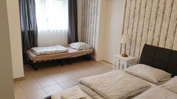 Ein kleines, ordentliches Zimmer mit zwei Betten, einem Nachttisch und einem Fenster mit Vorhängen.