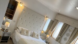 Una cama grande con cabecera capitonada, una mesita de noche, una lámpara y un espejo.