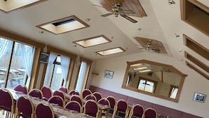 Un comedor con varias mesas y sillas, ventanas amplias y ventiladores de techo.