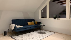 Un dormitorio estilo loft acogedor con un sofá azul, una mesita redonda pequeña y una alfombra estampada.