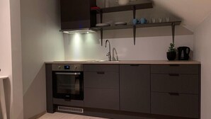 Una cocina moderna con horno empotrado, lavamanos y microondas. Hay armarios y una encimera con una planta y un hervidor.