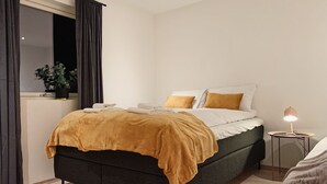 Un dormitorio moderno con cama, lámpara de noche y ventana con cortinas.