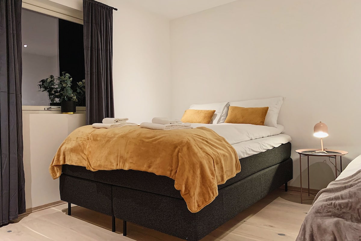 A modern bedroom with a bed, a bedside lamp, and a window with curtains.