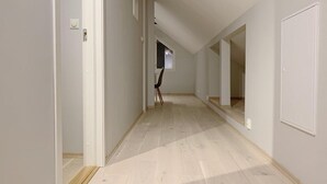 Un pasillo con suelo de madera, paredes blancas y una puerta a la izquierda.