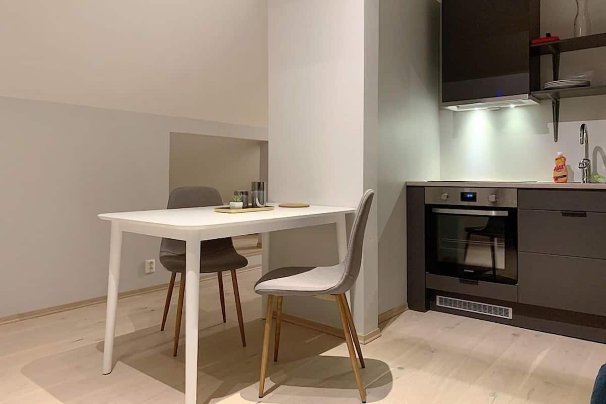 A modern kitchen with a white table and two chairs, a built-in oven, and a dark cabinet with a light above it.