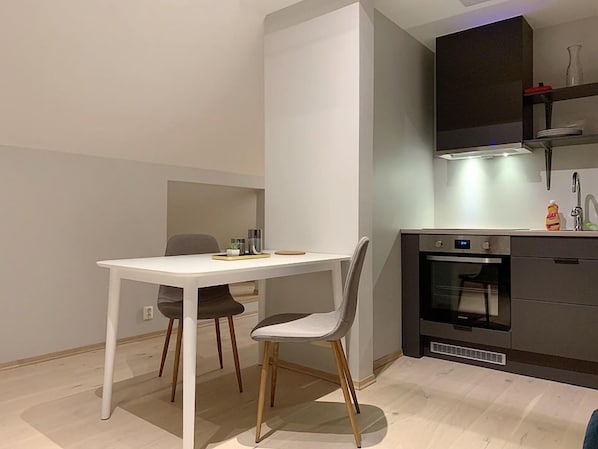 A modern kitchen with a white table and two chairs, a built-in oven, and a dark cabinet with a light above it.