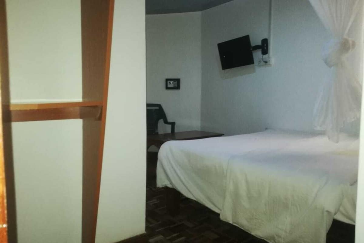Una habitación con una cama, un televisor montado en la pared y una silla.
