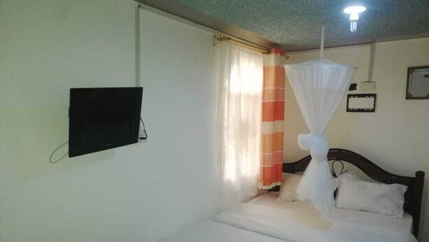 Een slaapkamer met een bed, een aan de muur bevestigde televisie en een gordijn met een strepenpatroon.