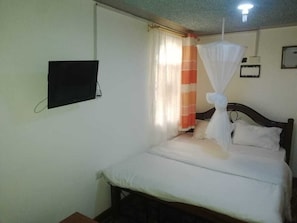 A bedroom with a bed, a television mounted on the wall, and a curtain with a striped pattern. - Guest House Hotel Chrisna - Hostel (Nairobi)