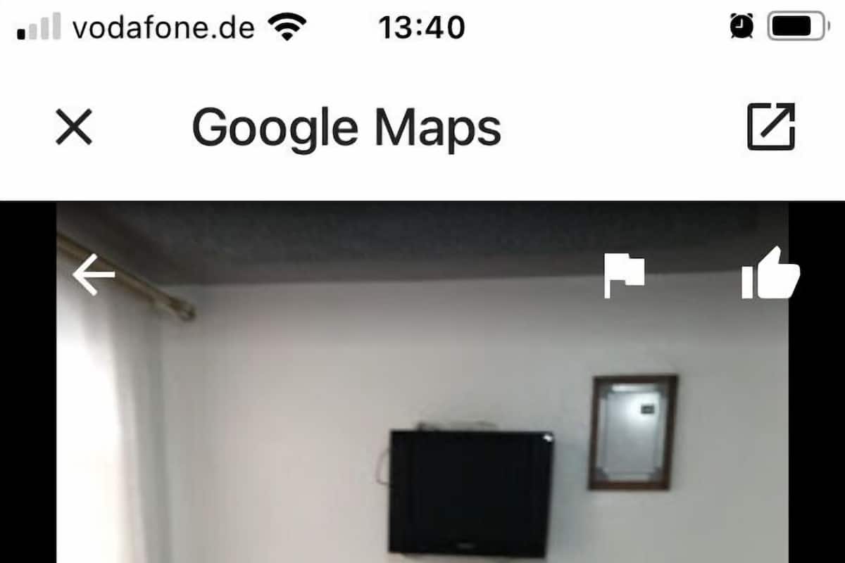 Una habitación con una cama, televisión en la pared y ventana con cortinas.