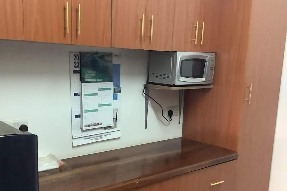 Una cocina con armarios de madera, microondas y un calendario en la pared.