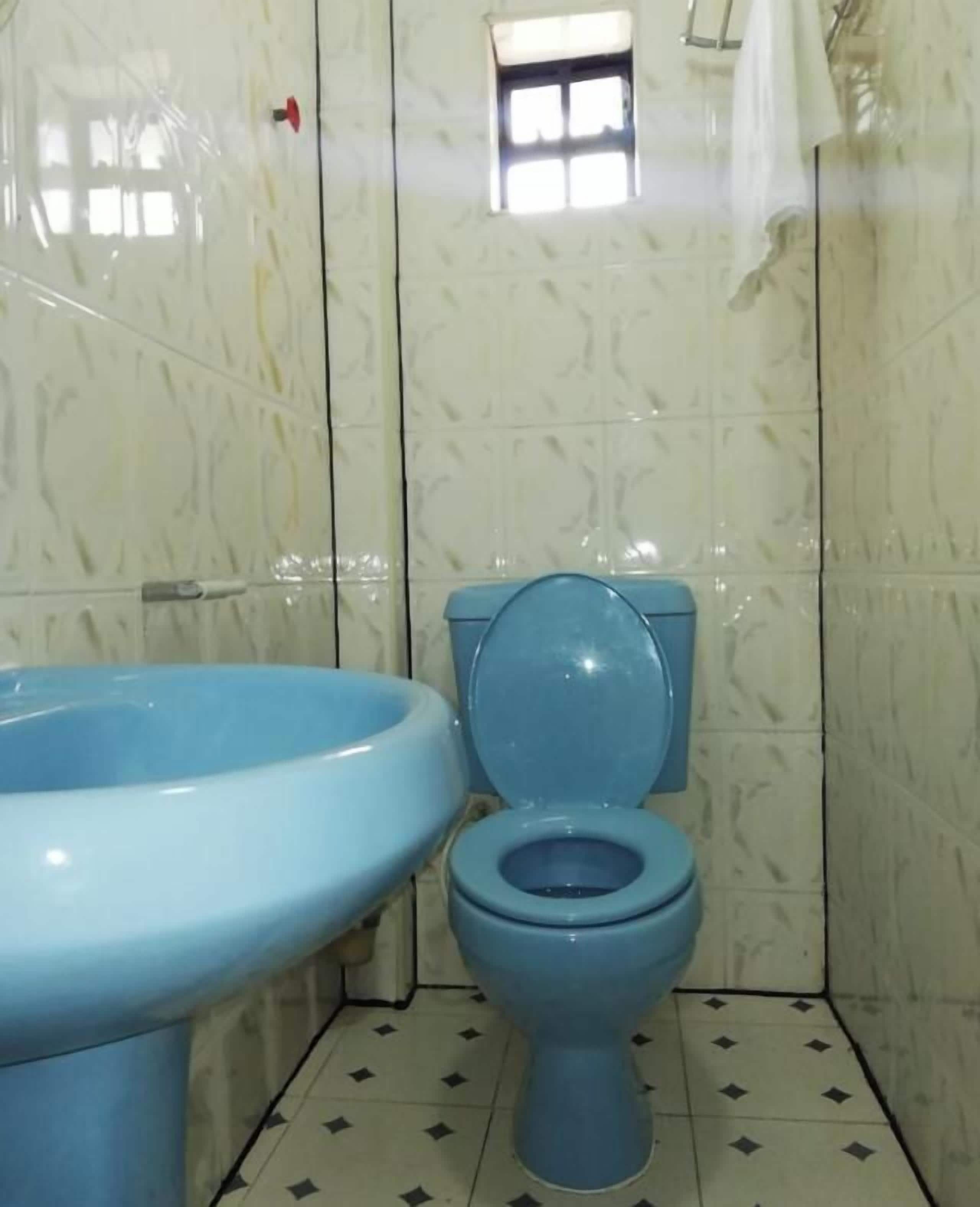 Ein Badezimmer mit Toilette und Waschbecken in Blau, geflieste Wände und einem kleinen Fenster.