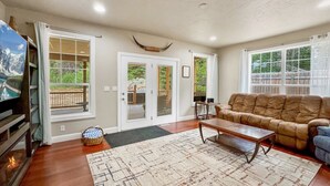 Un salon spacieux doté d’un plancher en bois, d’un grand tapis, d’un canapé et d’une table basse. On y trouve également une cheminée, un téléviseur et une porte donnant sur un balcon.