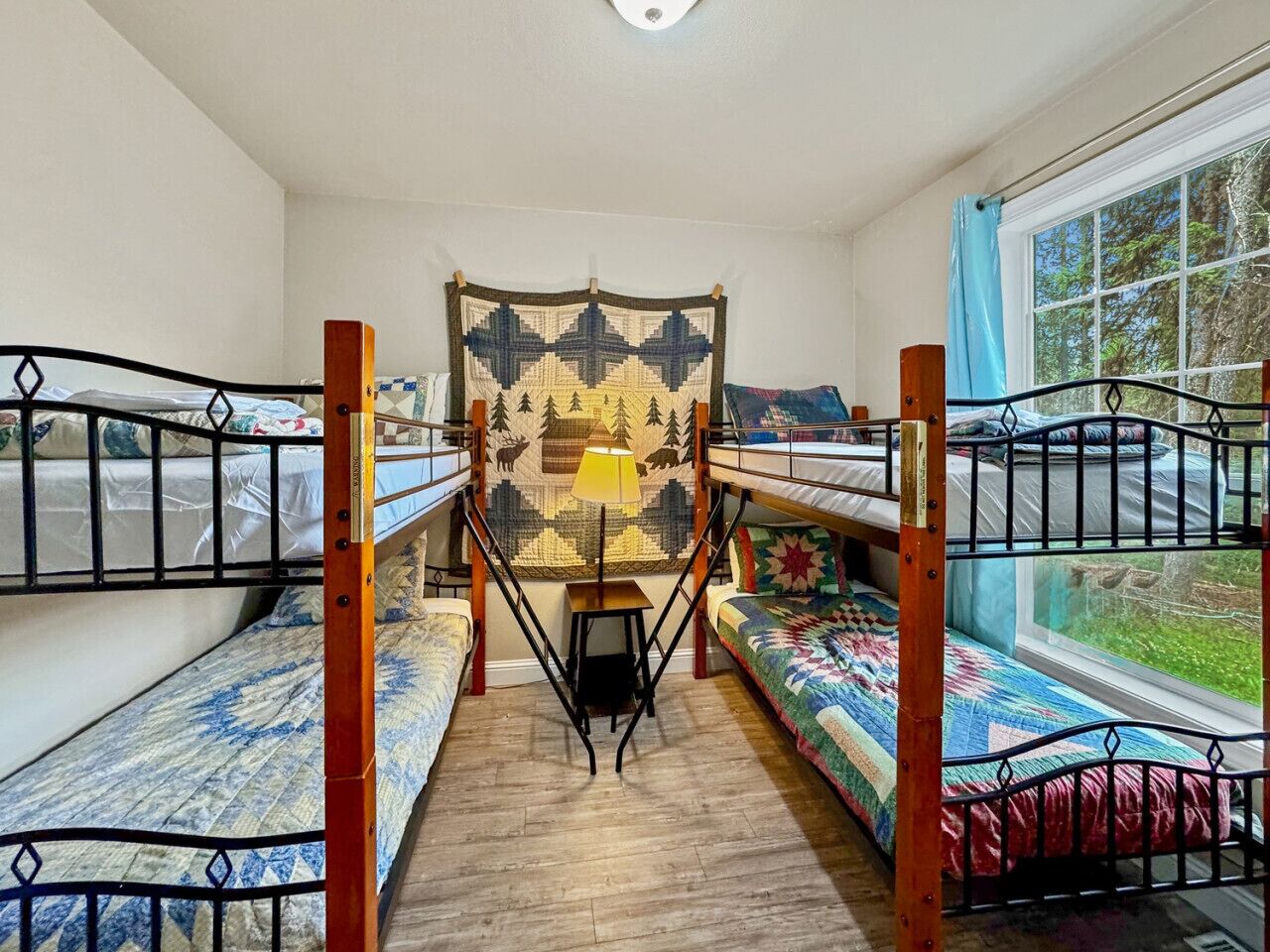 A dormitory room with bunk beds, a central table, and a window with a view of greenery.