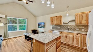 Une cuisine avec des meubles en bois, un îlot central doté d’un plan de travail en granit et un ventilateur de plafond.