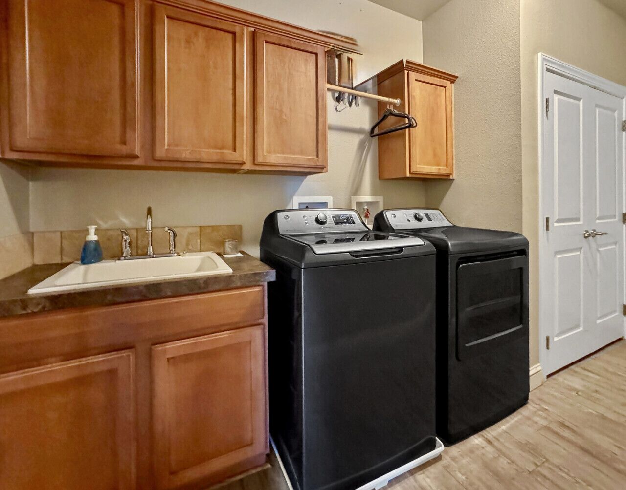 A laundry area with two black washing machines, a wooden countertop with a sink, and cabinets.