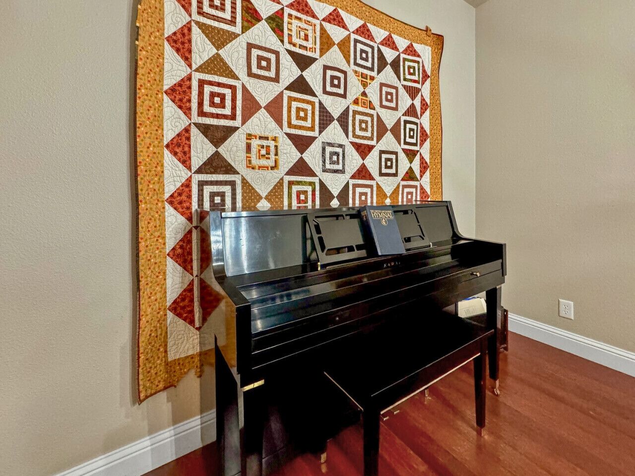 A piano in a room with a patterned wall hanging.