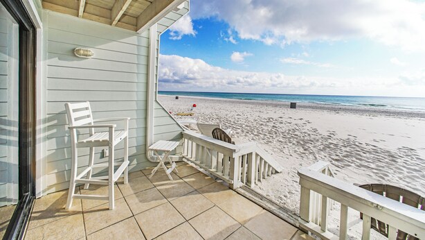 A beach view from a covered porch with white chairs and a small table.
