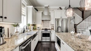 Een moderne keuken met witte kasten, granieten aanrechtbladen, roestvrijstalen apparatuur en een decoratieve kroonluchter.