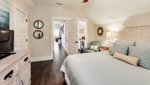 Een slaapkamer met een bed, een plafondventilator, een dressoir, een televisie en een gang naar een andere kamer.