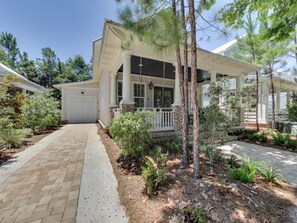 Ein zweistöckiges Haus mit überdachter Veranda, Garage und einem angelegten Garten mit verschiedenen Pflanzen und Bäumen.