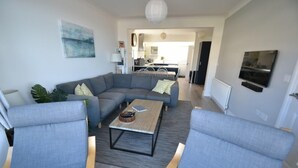 A modern living room with a grey sectional sofa, two armchairs, a coffee table, and a TV mounted on the wall.