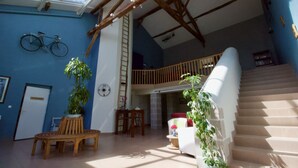 A spacious living area with a high ceiling, wooden beams, a staircase, and a skylight.